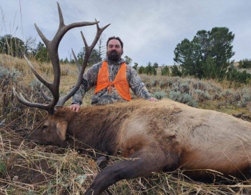 Hunter posing with his bull elk on a hillside in Wyoming